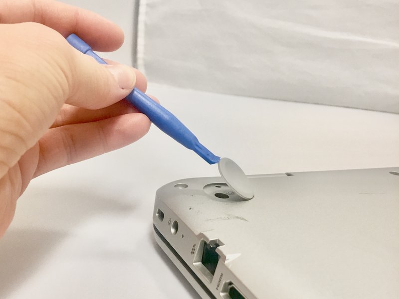 Image of a plastic opening tool prying off a rubber pad from the HP laptop.
